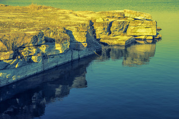 Limestone stone shore in an old quarry with reflection in the water. Tinted in yellow with blue.