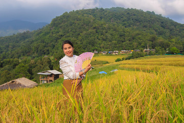 A woman dressed in Lanna dress, holding folding fan in a rice field on a mountain in Pongpang forest, Mae Chaem, Chiang Mai
