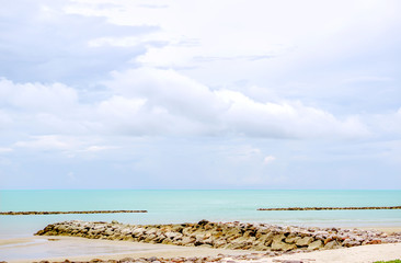 Rock mound on the beach with beautiful green sea under the light blue sky.