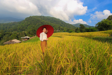 A woman dressed in Lanna dress, holding an umbrella in a rice field on a mountain in Pongpang forest, Mae Chaem, Chiang Mai