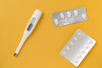 Thermometer and blisters of pills on a bright yellow background. Flat lay, top view. Pharmacy and medical concept