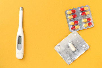 Thermometer and blisters of pills on a bright yellow background. Flat lay, top view. Pharmacy and medical concept