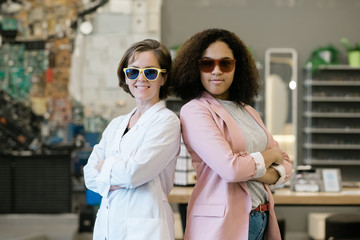 Two young multicultural females in sunglasses standing close to each other