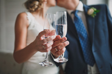 Close up crop bride and groom are holding glasses with a drink. Selective focus.