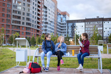 Teen girls eat on a bench in a city park.