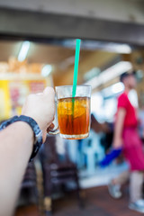 Hand holding ice tea in a glass with straw