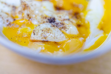 Soft boiled egg cracked open in a bowl with a hint of black pepper
