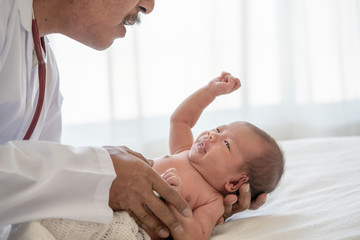 Fototapeta na wymiar Crying asian newborn baby girl check up examines by pediatrician doctor. Happy male doctor hand using stethoscope examining little cute baby infant heart and lung in clinic. Baby health care concept.