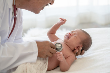 Crying asian newborn baby girl check up examines by pediatrician doctor. Happy male doctor hand using stethoscope examining little cute baby infant heart and lung in clinic. Baby health care concept.