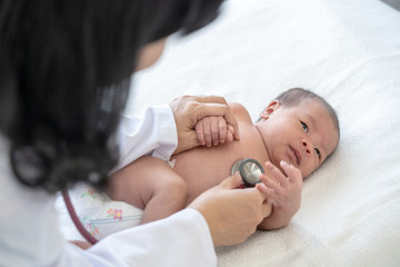 Obraz na płótnie Canvas Adorable asian newborn baby girl check up examines by pediatrician doctor. Female doctor hand using stethoscope examining little cute baby infant heart and lung in clinic. Baby health care concept.