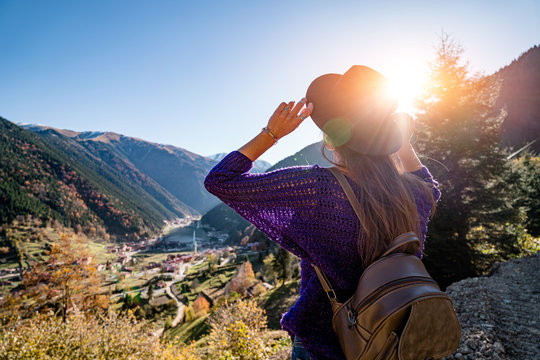 Stylish trendy hipster woman traveler in a felt hat with brown backpack stands on the background of the mountains and uzungol lake in Trabzon during Turkey travel