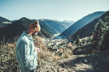 Naklejka premium Stylish trendy hipster man traveler in a yellow hat and denim jacket stands on a background of the mountains and uzungol lake in Trabzon during Turkey travel