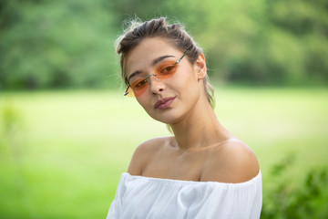 Fashion portrait of a pretty smiling woman in glasses against park