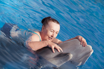 Happy elderly woman swims with a dolphin in the pool