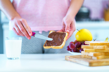 Woman spreads nut chocolate cream on toast bread for a dessert at home