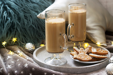Homemade latte in glass cups, served with gingerbread on the background of plaid, pillows and garlands.
