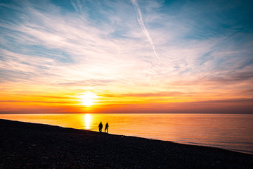 Fototapeta premium Silhouettes of loving couple walking along the seashore at sunset