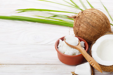 Background of coconut, coconut shell, oil in clay bowl and spoon on white wooden table