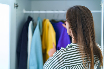 Naklejka na ściany i meble Brunette woman choosing outfit from wardrobe closet with stylish clothes and home stuff