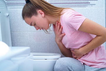 Young woman suffers from nausea and vomiting due to digestive and stomach illness problems at...