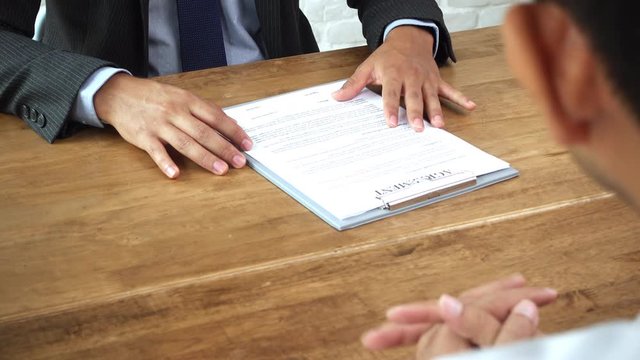 Businessman offering bribe money in envelope together with contract agreement paper to his partner to sign at the table