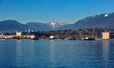 Naklejka premium The ships under loading in the sea port of North Vancouver on the background of mountain range and blue sky