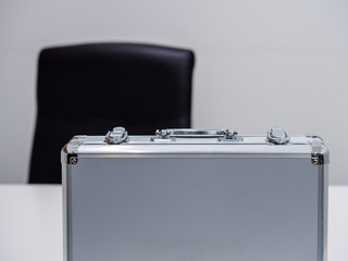 Close up of an upright metal briefcase on a table in an office setting. Business deal / cash transaction concept