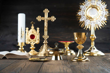 Roman Catholic Church theme. The Cross, Holy Bible, monstrance, rosary and golden chalice on rustic wooden table.