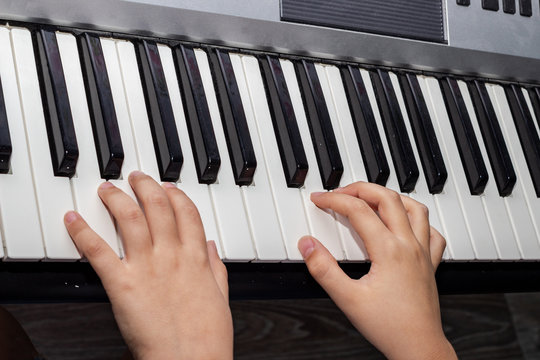 Close up of baby's hands playing the piano. Hands of a child playing the keyboard of a synthesizer. A closeup image of a baby's hand and black and white piano keys.
