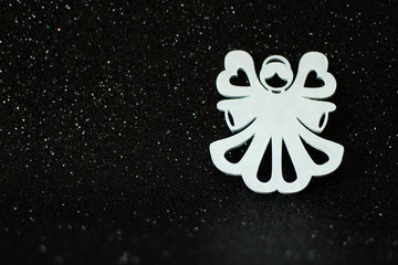 Simple Christmas or winter concept: white, decorative angel, located on the right side, black glitter background, selective focus, free copy space