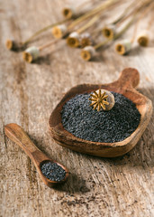 Rustic wooden bowl with poppy seeds and dry poppies pods. Selective focus.