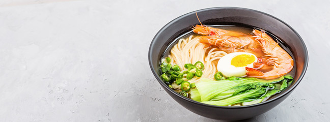 Asian noodle soup, ramen with prawn shrimp, vegetables and egg in black bowl on gray concrete background. Flat lay, Top view, mock up, overhead. Healthy food concept