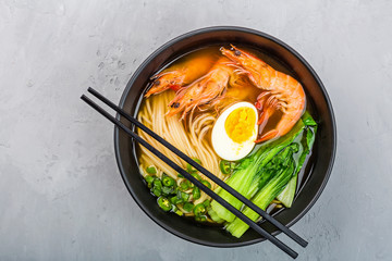 Asian noodle soup, ramen with prawn shrimp, vegetables and egg in black bowl on gray concrete background. Flat lay, Top view, mock up, overhead. Healthy food concept