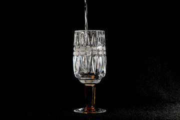 White wine pours into a crystal glass on a black background.