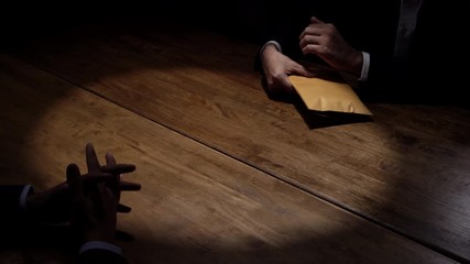 Businessman rejecting money in the envelope secretly offered by his partner in dark room, anti bribery corruption concept