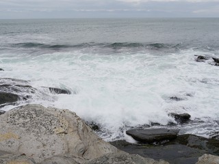 Foaming white waves break on to the big rocks in a shoreline