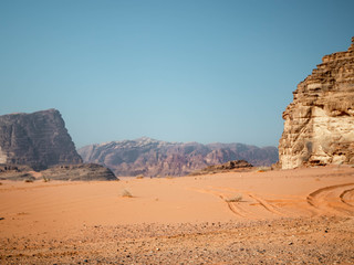 Rocky outcrop in the desert of Wadi Rum in the morning with tyre tracks in the sand