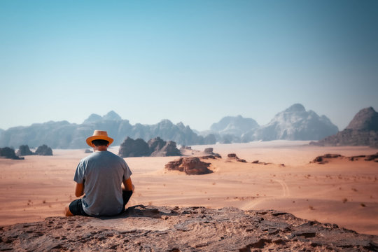 Guy sitting on a rocky outcrop in the desert of Wadi Rum with mountains in the background