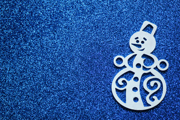 Simple winter concept: white snowman, located on the right side, blue glitter background, selective focus, free copy space