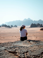 Girl sitting on a rocky outcrop in the desert of Wadi Rum with mountains in the background