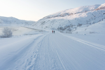 two girls in bright jackets walk along a white snowy road through the tundra beyond the Arctic Circle on a frosty clear day