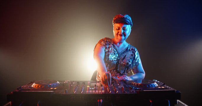 Authentic grandma DJ with shiny clothes and makeup performing in a nightclub with neon lights 4k footage