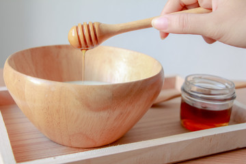 Pouring honey on yogurt in wooden bowl.