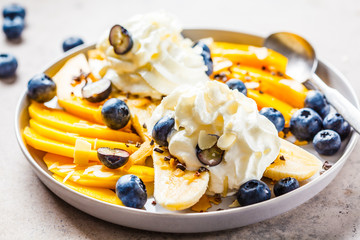 Healthy banana split with mango, chocolate and whipped cream on gray plate.