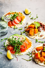 Open vegan tortilla wraps with sweet potato, beans, avocado, tomatoes, pumpkin and  sprouts on gray background, flat lay, copy space. Healthy vegan food concept.