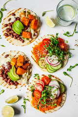 Open vegan tortilla wraps with sweet potato, beans, avocado, tomatoes, pumpkin and  sprouts on...