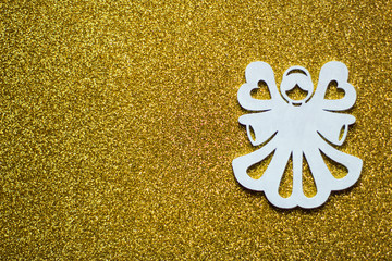 Simple Christmas or winter concept: white, decorative angel, located on the right side, golden glitter background, selective focus, free copy space