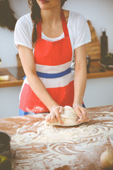 Obraz na płótnie Canvas Young brunette woman cooking pizza or handmade pasta in the kitchen. Housewife preparing dough on wooden table. Dieting, food and health concept