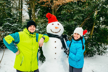 couple posing near big snowman in red hat