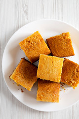 Homemade Sliced Cornbread Ready to Eat on a white plate on a white wooden background, top view. Flat lay, overhead, from above. Closeup.